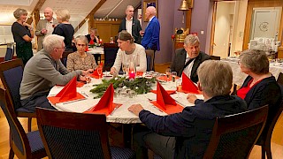 6 personer rundt et julebord og 5 personer står bakenfor og prater