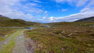 Landskap blå himmel med noen skyer, fjell og vei.